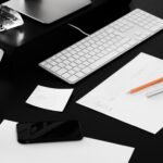 Web designer's workspace featuring a laptop, keyboard, design sketches, smartphone, and creative planning materials on a desk.