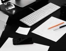 Web designer's workspace featuring a laptop, keyboard, design sketches, smartphone, and creative planning materials on a desk.