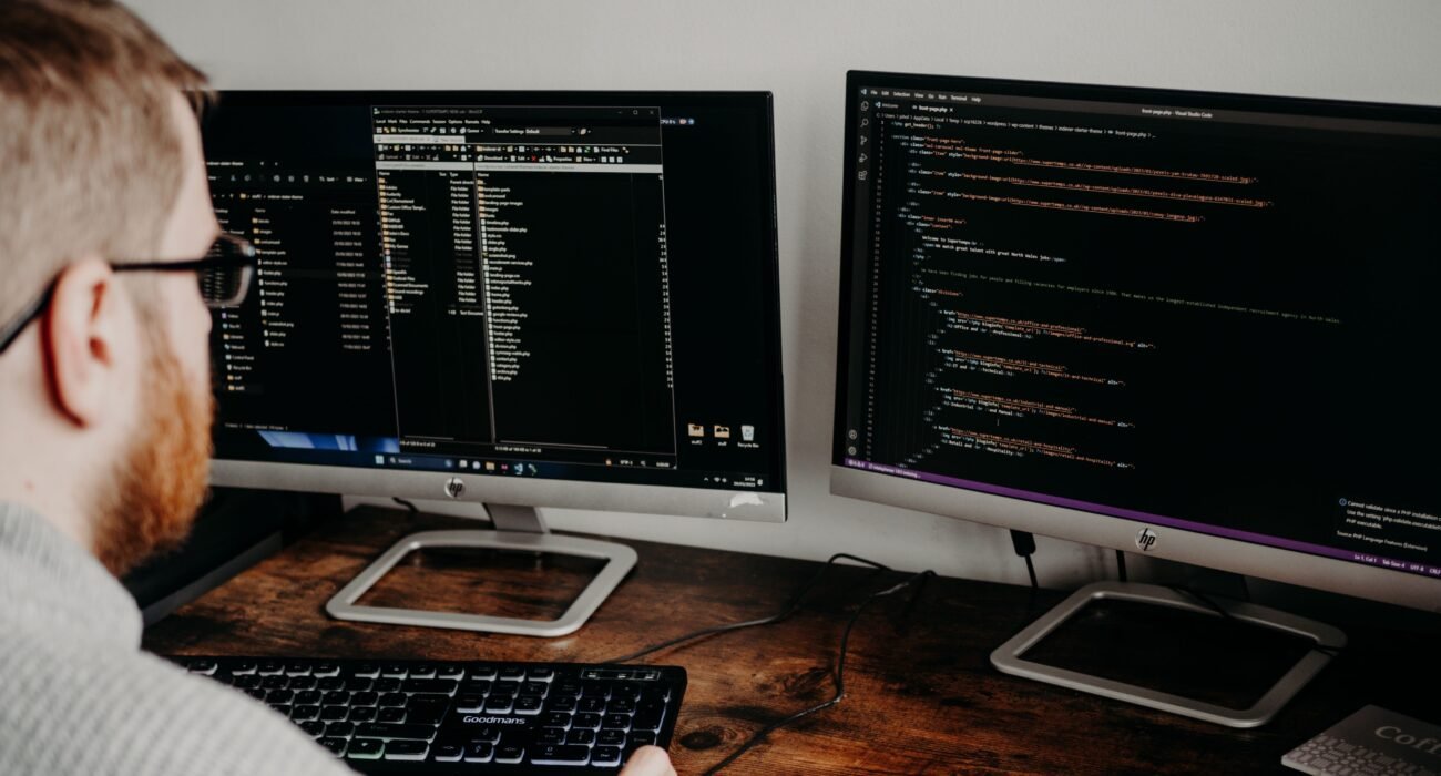 Software developer working at a desk with two monitors displaying code on dark screens.