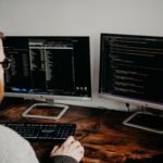Software developer working at a desk with two monitors displaying code on dark screens.
