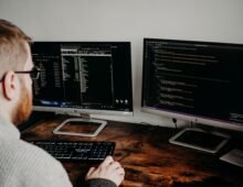 Software developer working at a desk with two monitors displaying code on dark screens.