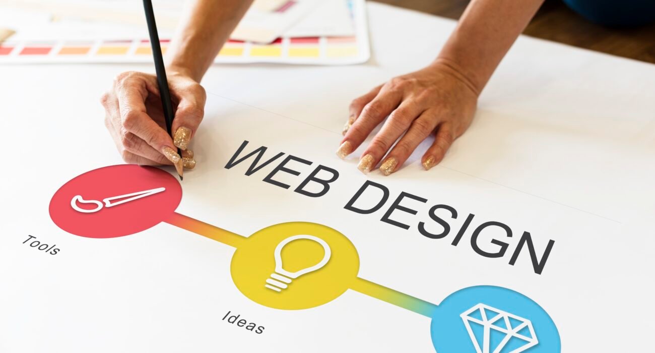 Designer planning a web design concept on paper with colorful icons representing tools, ideas, and creativity.
