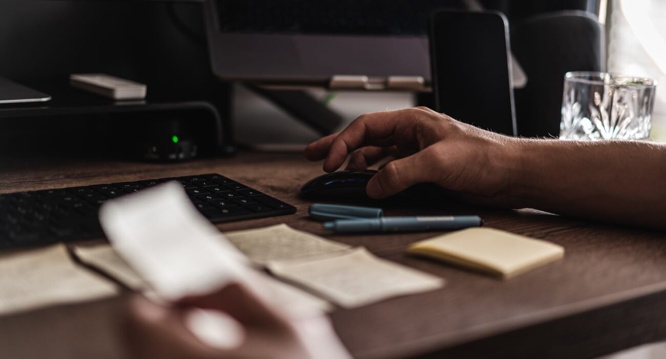 Web designer working at a computer desk with a keyboard, mouse, notes, and design materials.