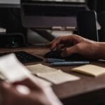 Web designer working at a computer desk with a keyboard, mouse, notes, and design materials.