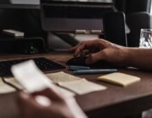 Web designer working at a computer desk with a keyboard, mouse, notes, and design materials.